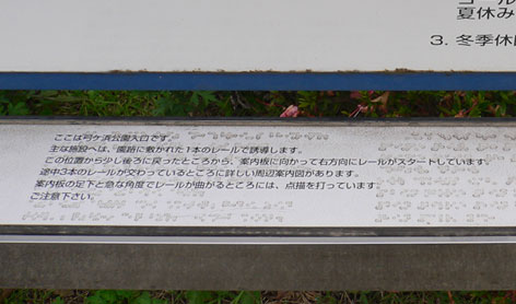 写真:点字の案内。「主な施設へは園路に敷かれた一本のレールで誘導します」と書いてある
