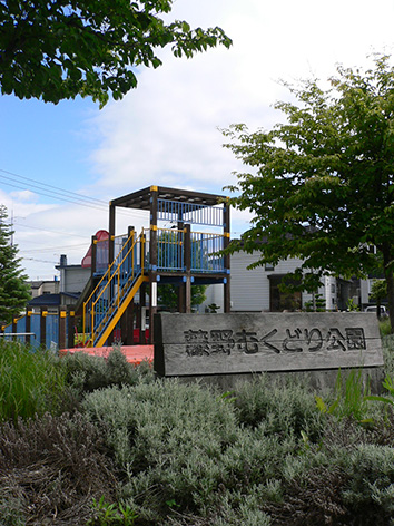 写真:公園の入り口。「藤野むくどり公園」と書かれた木の看板の背後に複合遊具