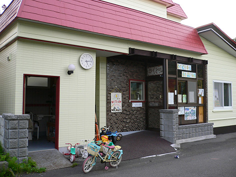 写真:むくどりホームの入口。子どもの三輪車などが置かれ、壁には「あいています」の手作りタペストリーが掛かる。手前は柴川さんが子どもたちのために作られた多目的トイレ