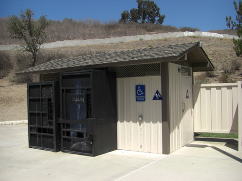 写真:トイレの建物の外に並んだ黒い大型の箱。隣には車いすマークの看板