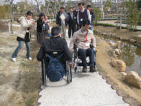 写真:UD調査の様子。小川への下り斜面脇の歩道を車いすですれ違うワークショップ参加者たち
