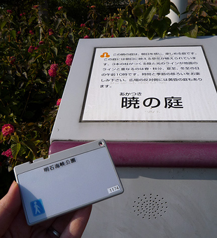 写真:案内板と音声案内用の無線カード。カードの大きさは、縦5センチ横9センチくらいで薄い。角の側面にスライドさせる小さなボタンが付いている