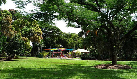 写真:緑いっぱいの公園の奥にあるカラフルな日除けや遊具